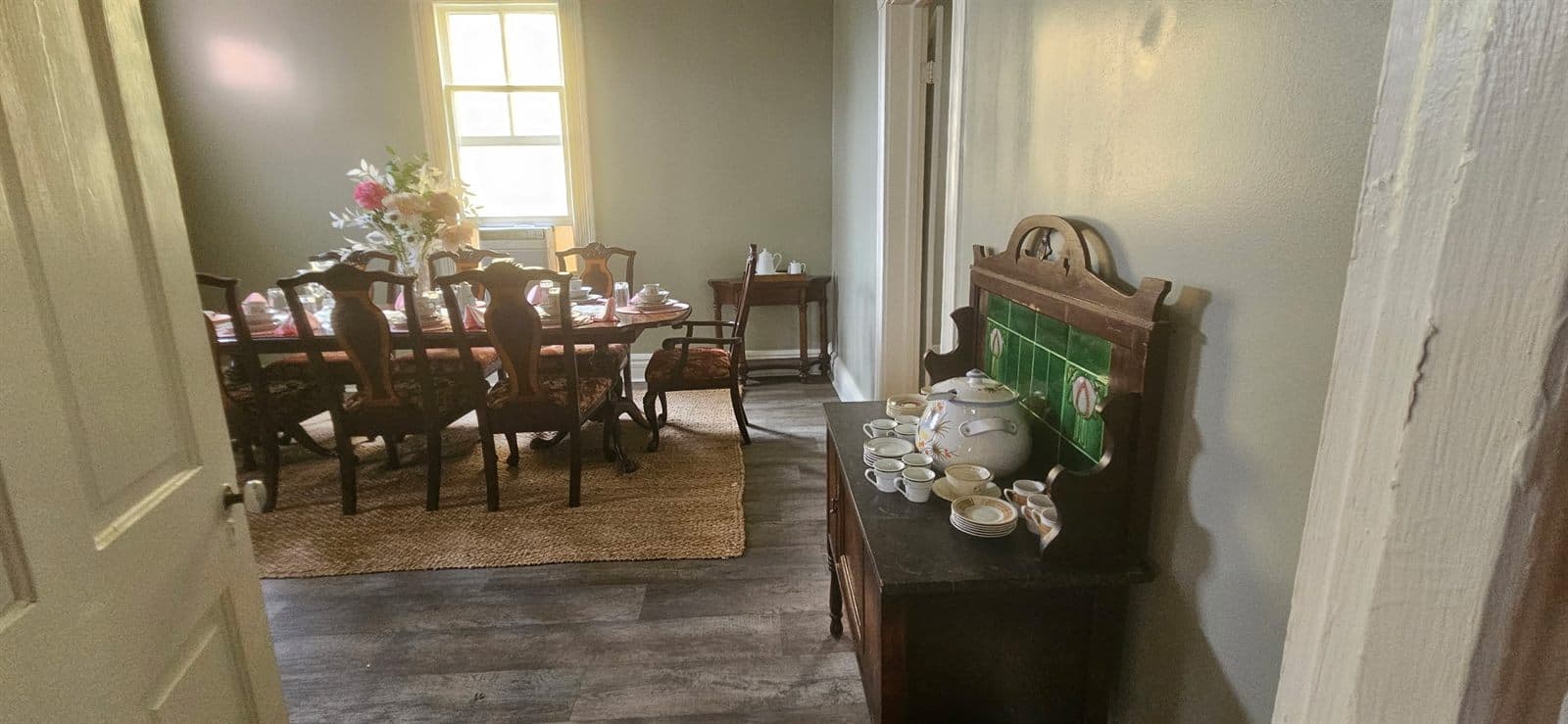 A dining room with an antique sideboard and warm natural light from the windows.