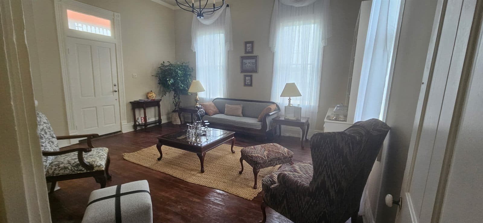 A bright parlor with comfortable seating gathered around a fireplace and tall windows.
