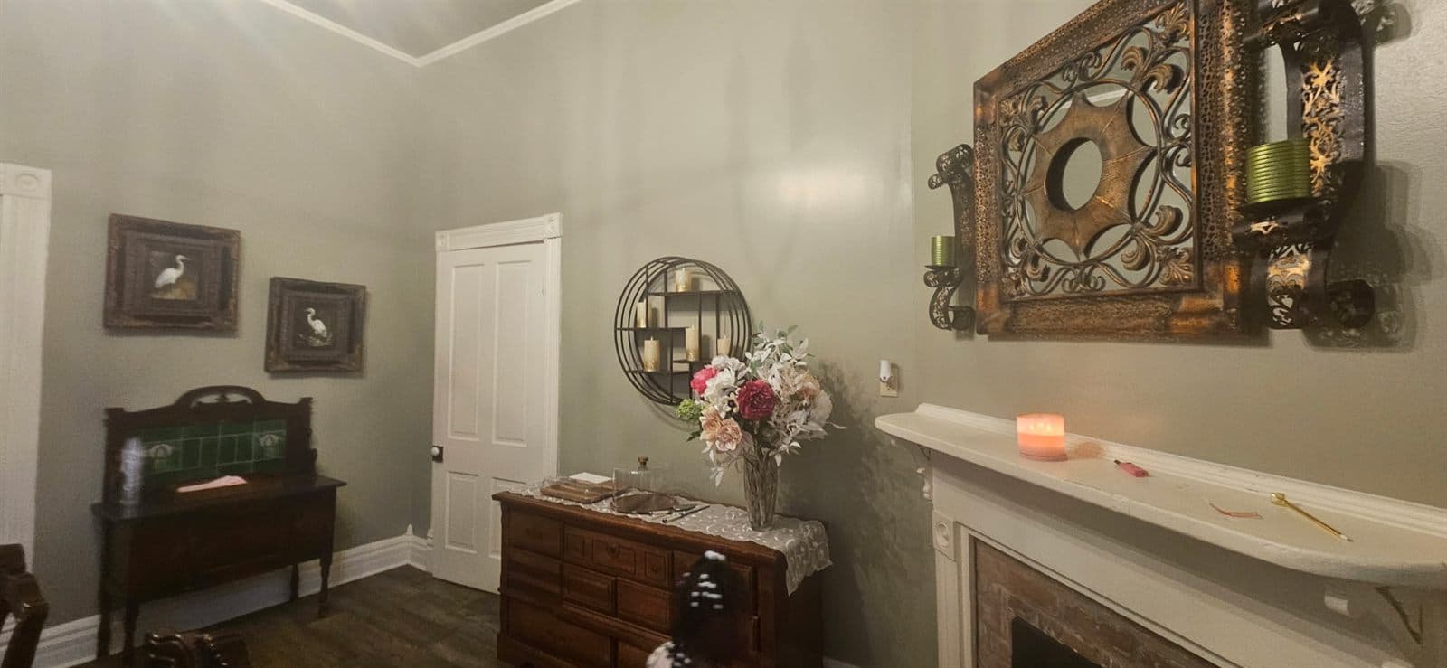 An interior parlor with an ornate mirror above a sideboard, candles, and floral arrangements.