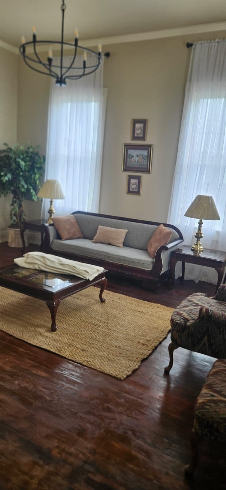 A warm sitting room with a sofa, wood floors, and a chandelier inside The Legacy at Madison.