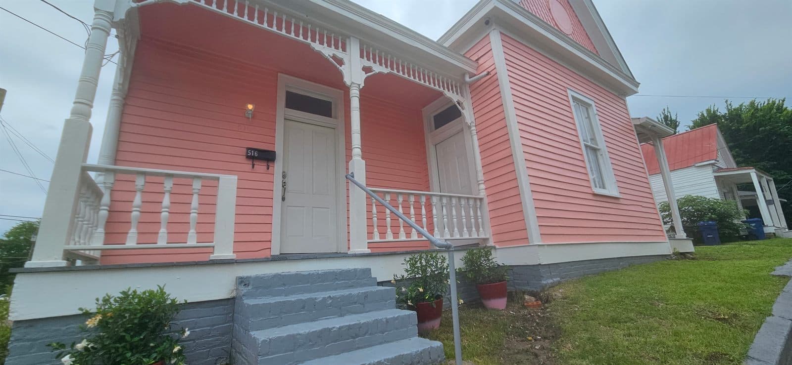 Side view of the pink house at The Legacy at Madison, showing its porch, columns, and front steps.